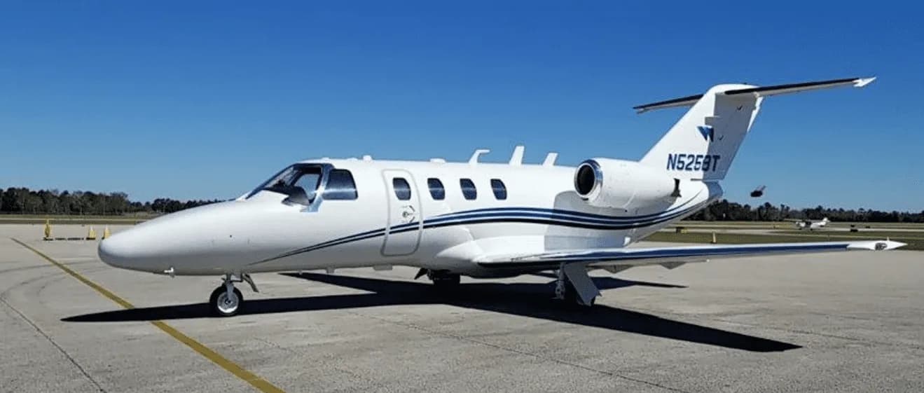 A white Cessna Citation CJ3 with blue stripes is parked on the tarmac.