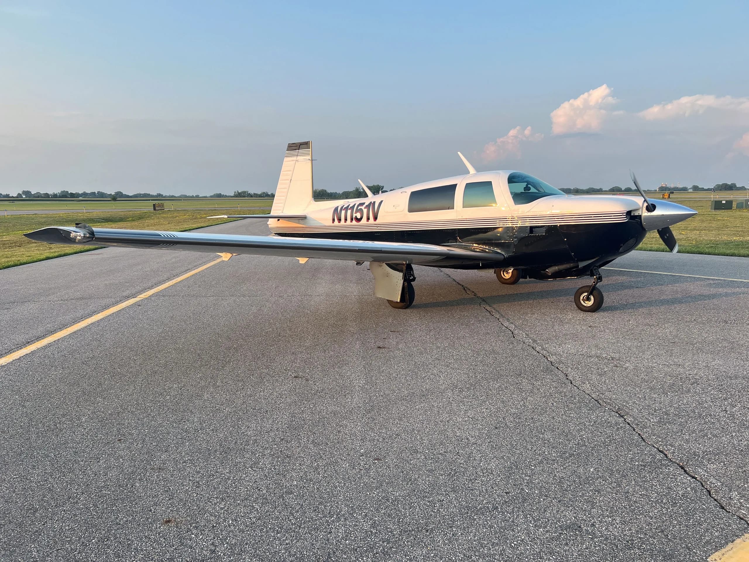 A white and dark blue single-engine aircraft, N1151V, with its wings extended, parked on an asphalt runway.