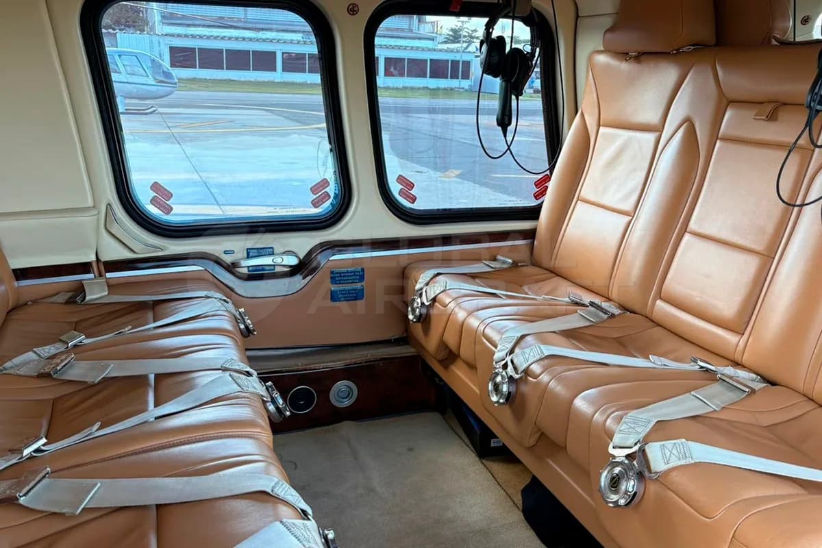 The interior cabin of a helicopter with two rows of brown leather seats and large windows.