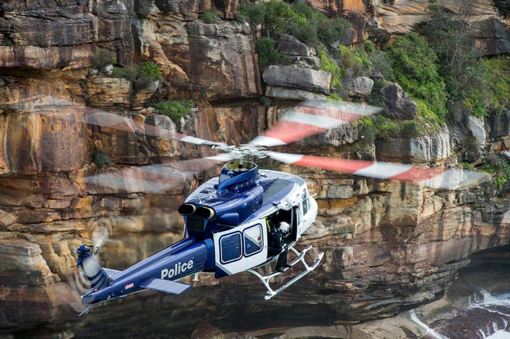 Blue and white police helicopter flying near cliffs.