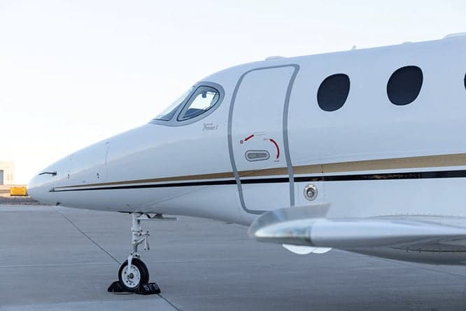 A close-up view of the nose and front cabin door of a white business jet with gold and black stripes.