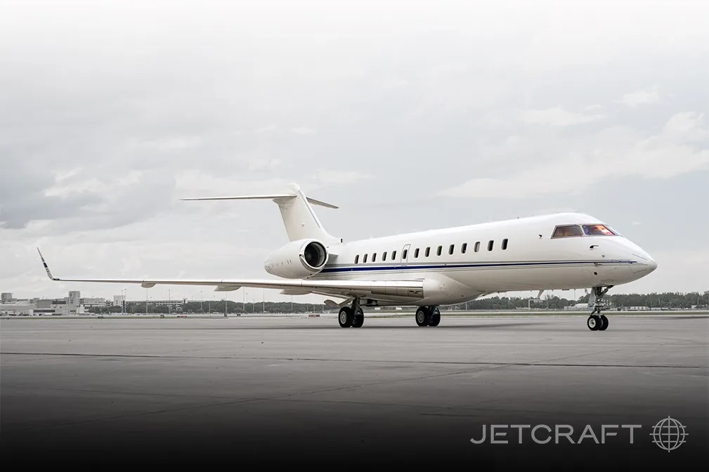 A white business jet with blue and grey stripes on the tarmac under a cloudy sky.