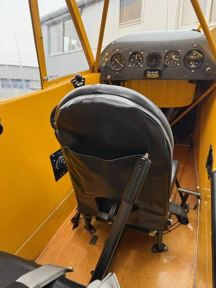 View of the black leather rear seat and wooden floor inside a yellow aircraft cabin, with a partial view of the instrument panel.