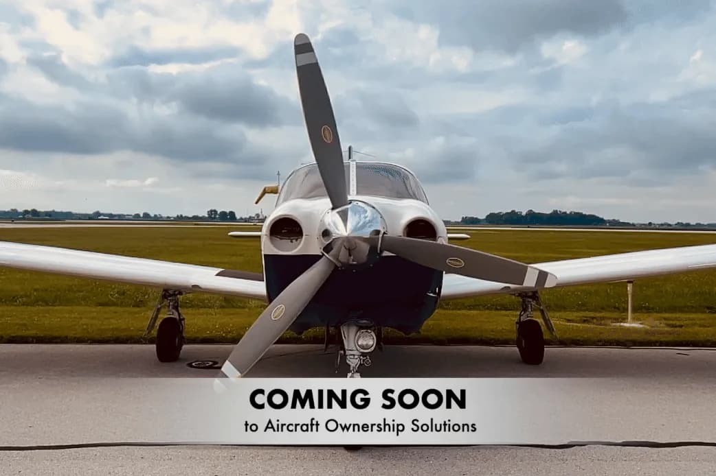 Front view of a white and blue twin-engine propeller aircraft parked on an airfield under a cloudy sky.