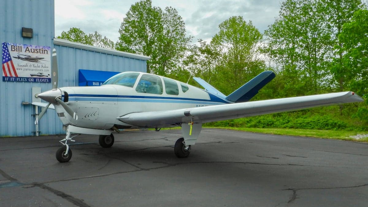 A white and blue Beechcraft Bonanza parked on the tarmac.