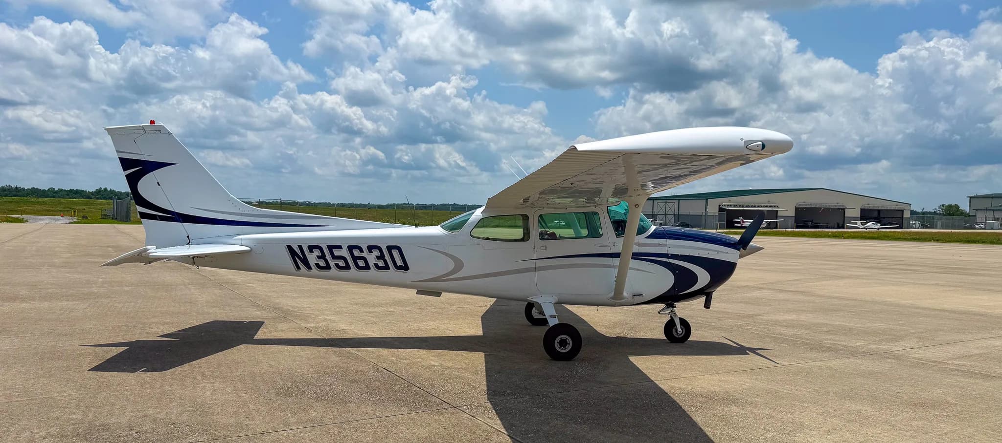 Left-rear view of a white and blue Cessna 172 with registration N3563Q on an airfield near a hangar.
