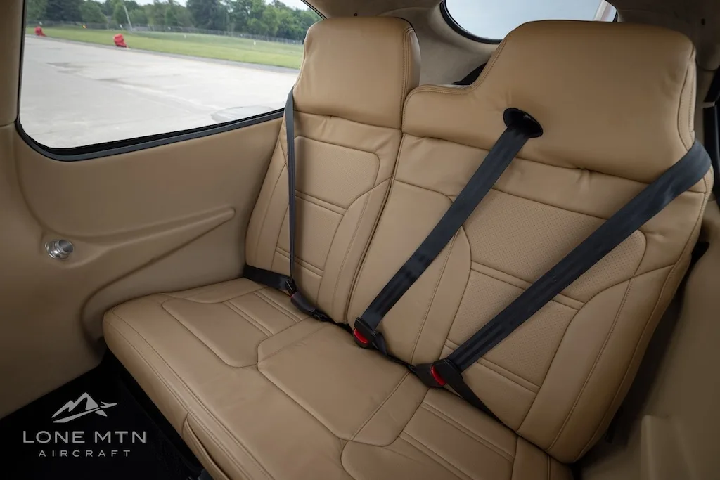 A close-up view of the tan leather rear seats with seatbelts in the aircraft cabin.
