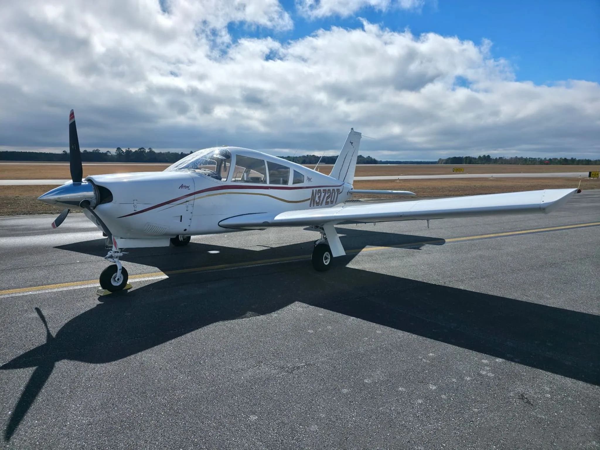 A three-quarter front view of the white Piper Arrow N3720T, showing the propeller and nose, parked on an airfield.