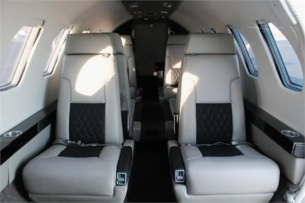 The interior cabin of a private jet features light gray and black leather seats with diamond stitching.
