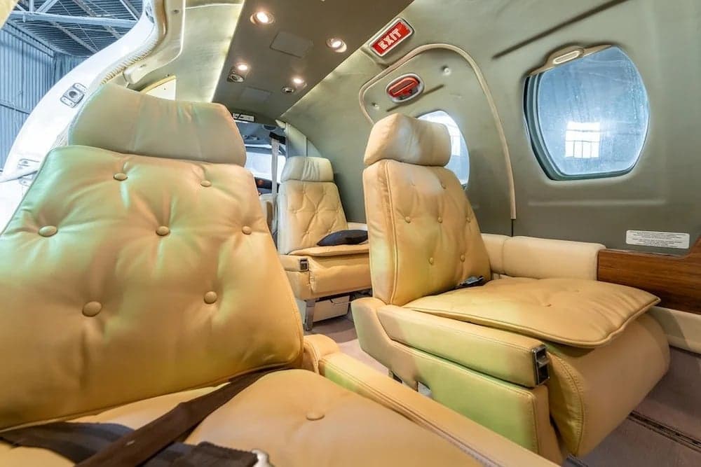 The interior of a Cessna Citation II features tan leather seats and an exit sign.