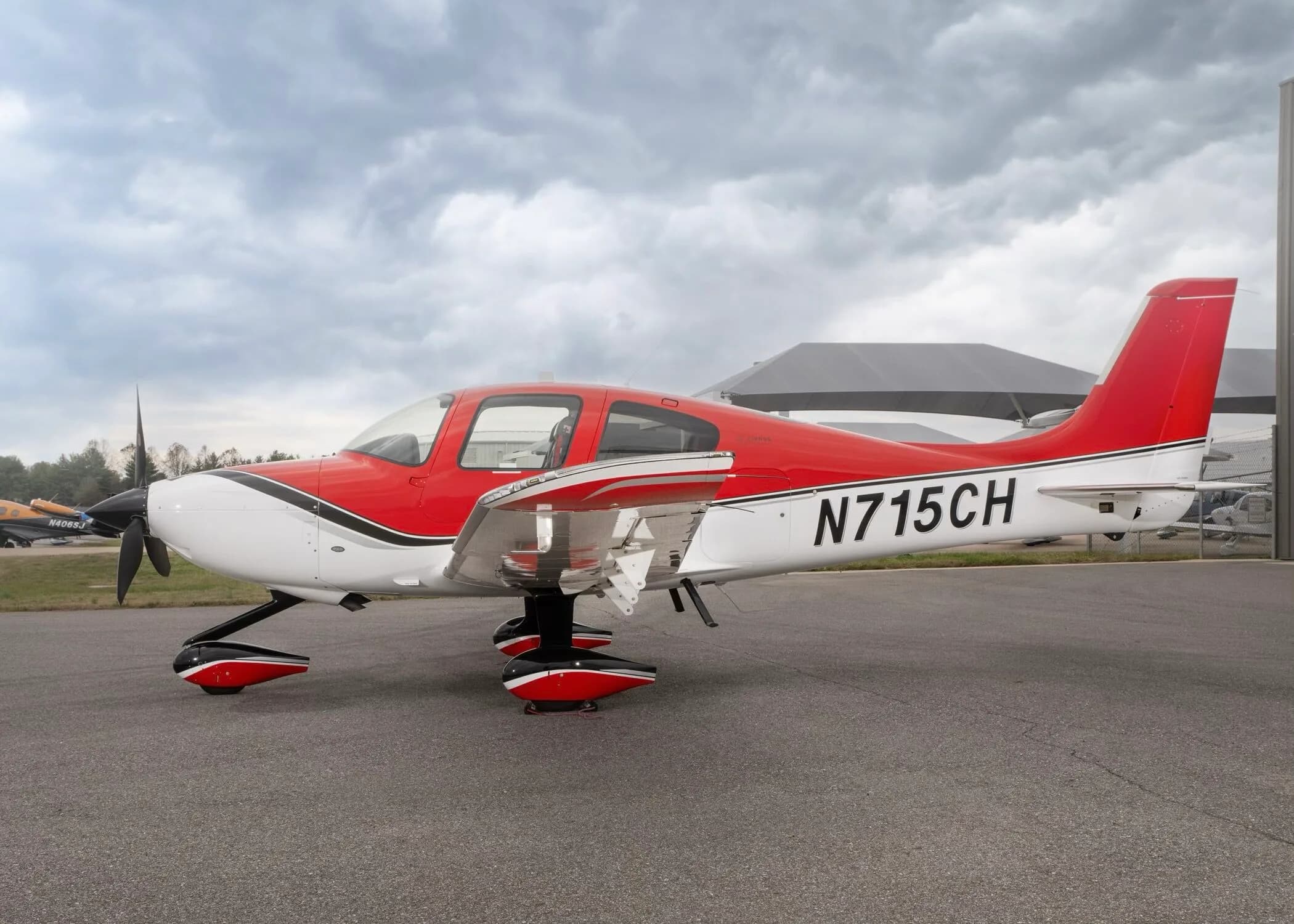 A red and white Cirrus SR22 aircraft with registration N715CH parked on an airfield under a cloudy sky.