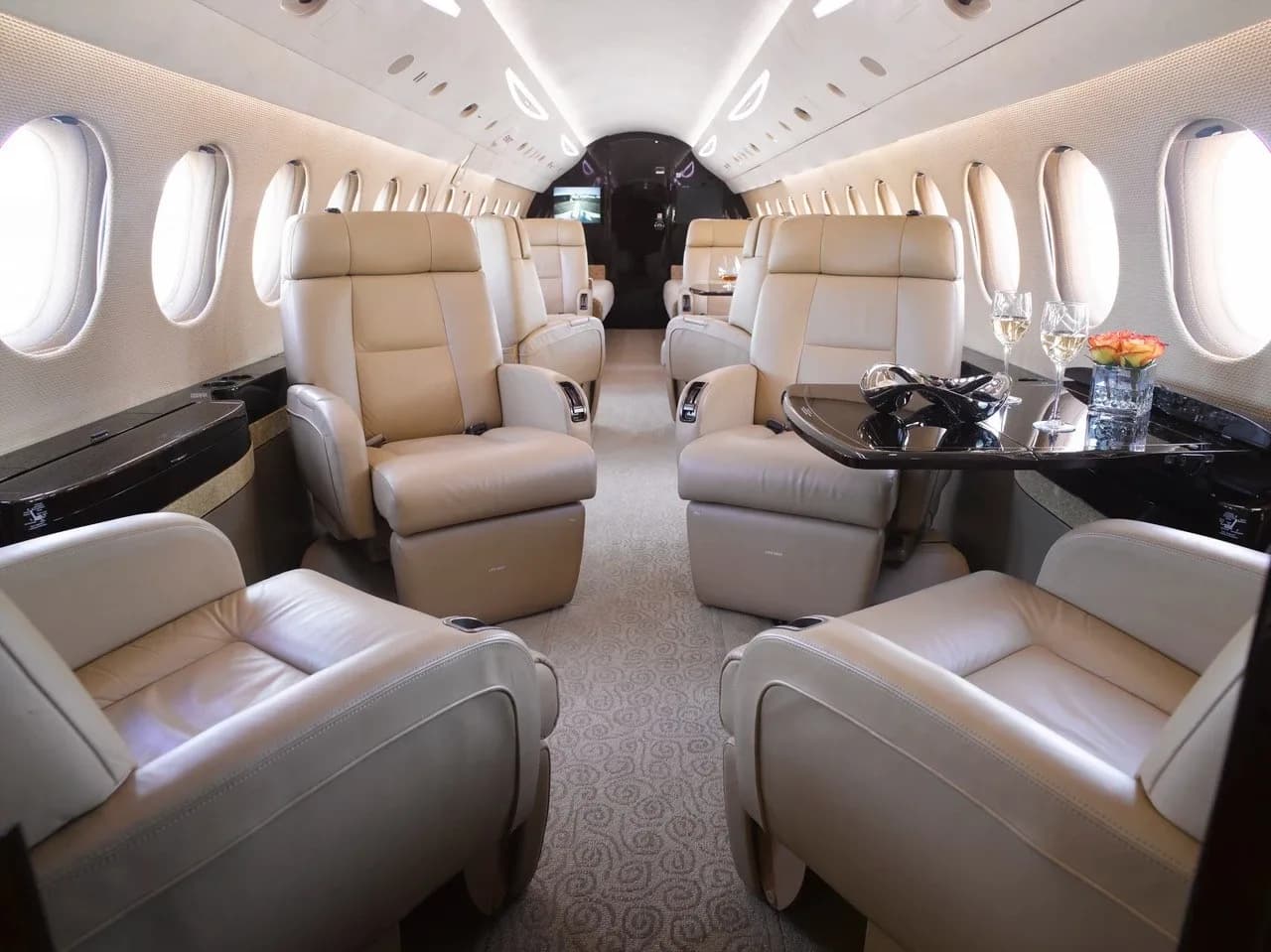 The luxurious main cabin of a private jet with beige leather seating and a table set with champagne glasses.