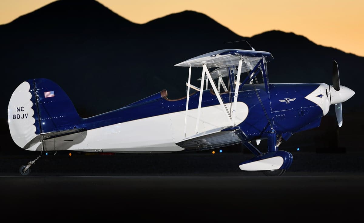 A blue and white biplane, N80JV, is parked on the tarmac at night.
