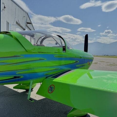 A green aircraft with blue accents parked on the tarmac in front of a hangar.