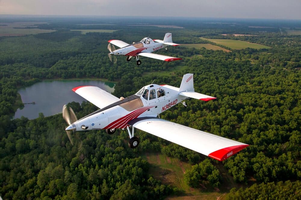 Two Thrush 510G aircraft flying in formation over a wooded area.