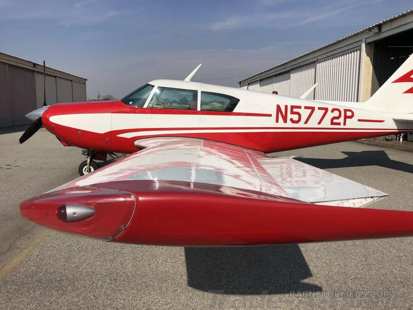 A red and white single-engine propeller aircraft with registration N5772P parked on an asphalt ramp in front of hangars.