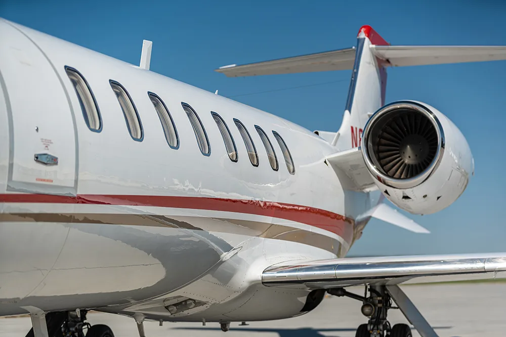 A close-up of the rear fuselage and engine of a white private jet with red and gold stripes.