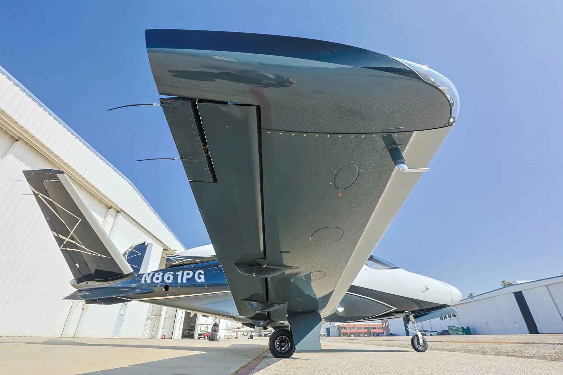Underside view of the right wing and fuselage of a Cirrus Vision Jet (N861PG) parked on an tarmac.