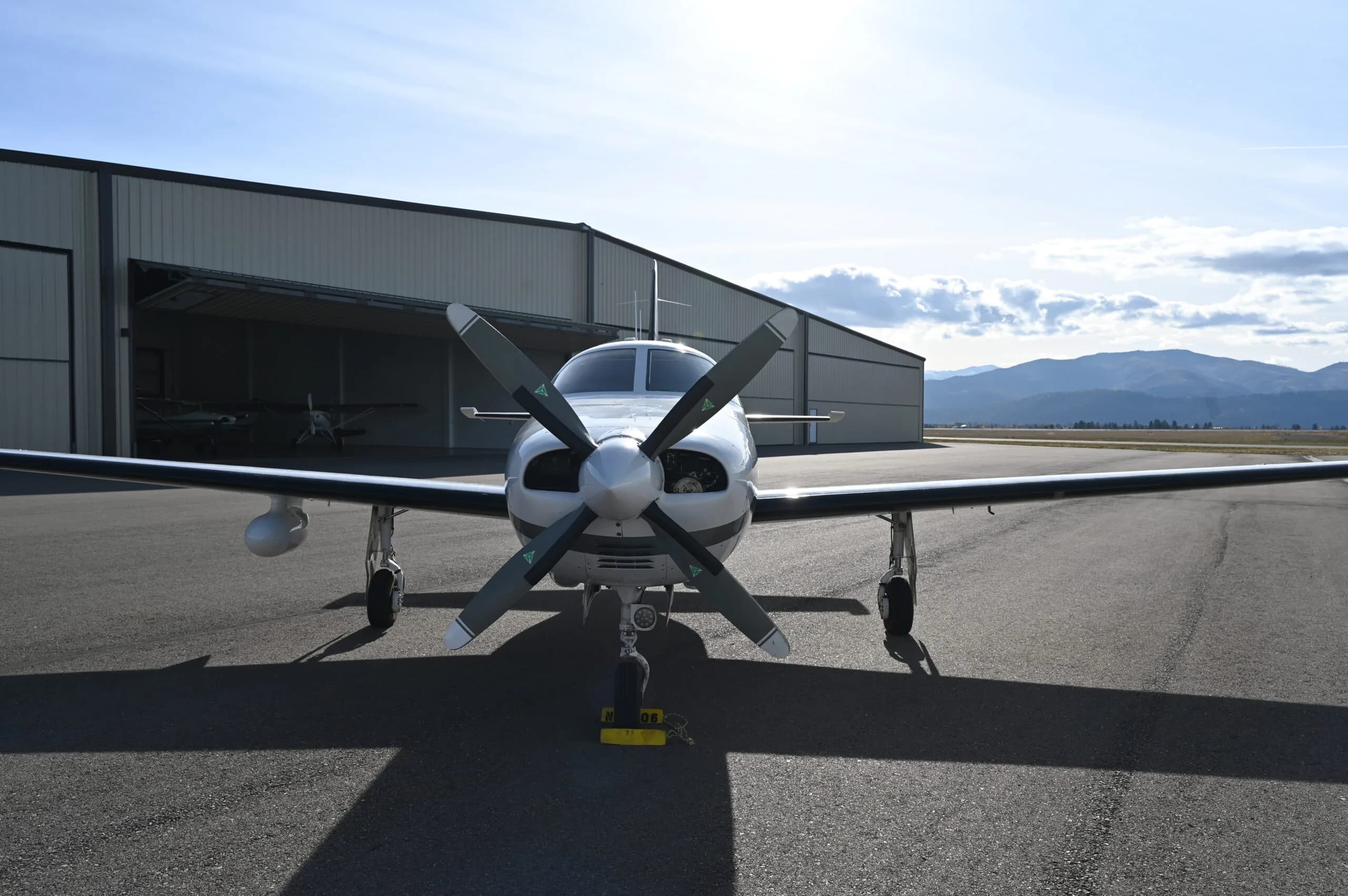 Front view of a Piper Mirage parked on the tarmac in front of a hangar with mountains in the background.