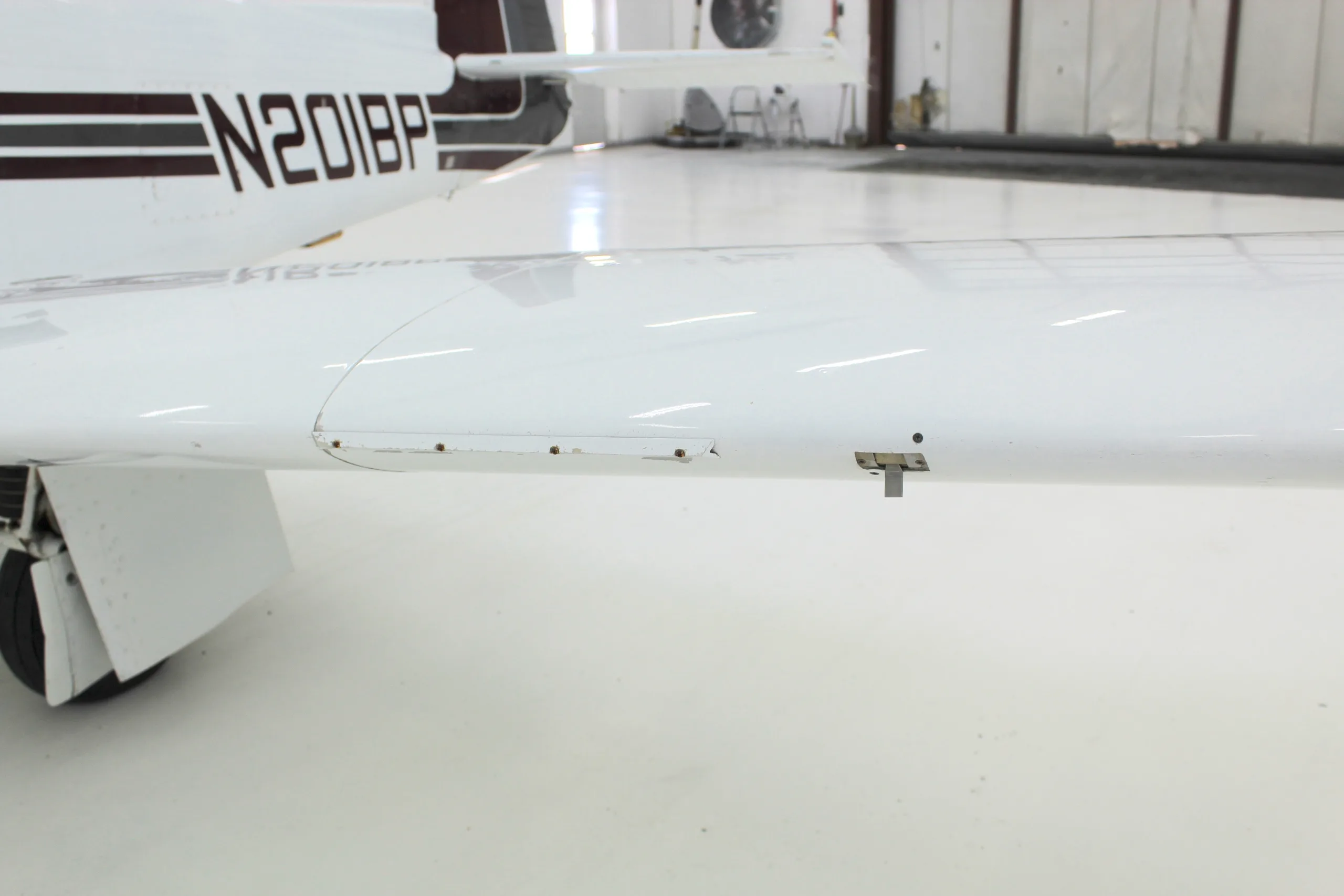 Close up of the wing of the white and brown N201BP aircraft in a hangar.