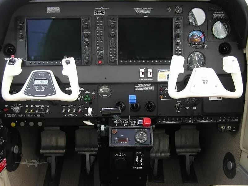 The cockpit of an aircraft featuring two large display screens, dual yokes, and various instruments and controls.