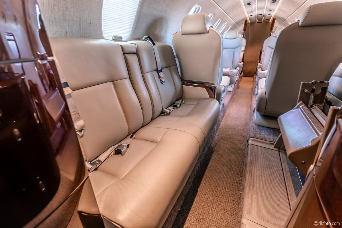 A close-up view of the light beige leather bench seating and aisle in the elegant interior of a private jet cabin.