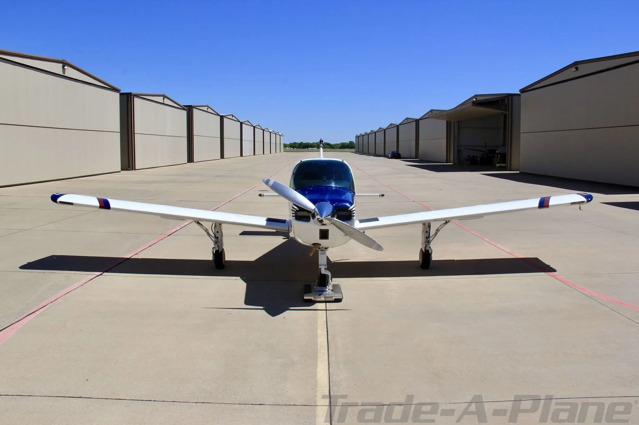 A head-on view of the white, blue, and red single-engine aircraft N66304, parked on an apron between hangars.