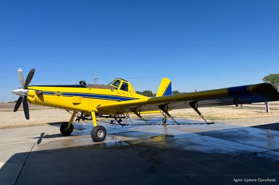 A yellow Air Tractor AT-802XP agricultural aircraft with blue stripes is parked on a tarmac under a clear blue sky.
