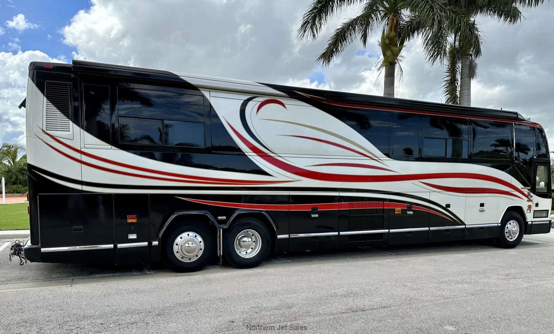 Side view of a Prevost coach with a black, white, and red paint scheme parked outside.