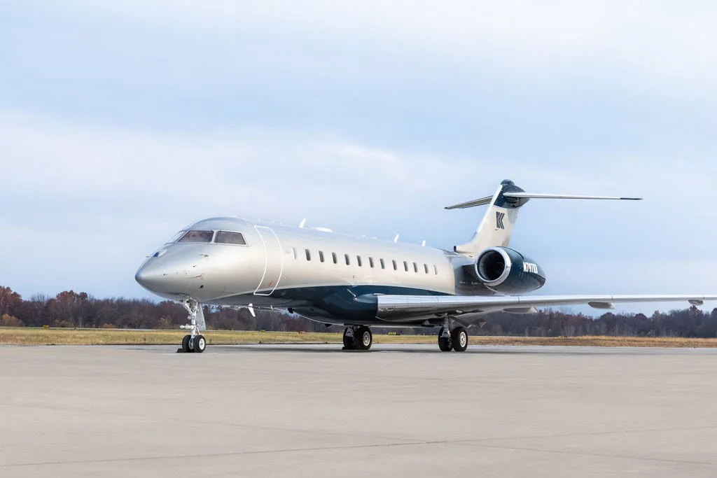 A silver and blue Bombardier Challenger business jet parked on a tarmac under a cloudy sky.
