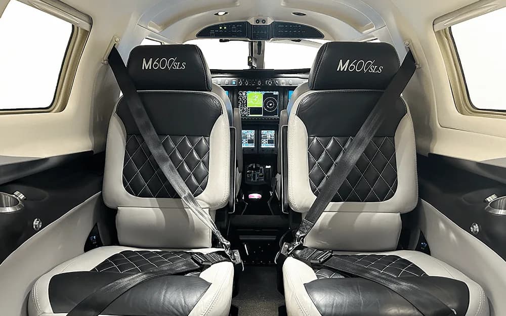 The luxurious black and white quilted leather front seats of the Piper M600/SLS cabin, with the cockpit instrument panel visible in the background.