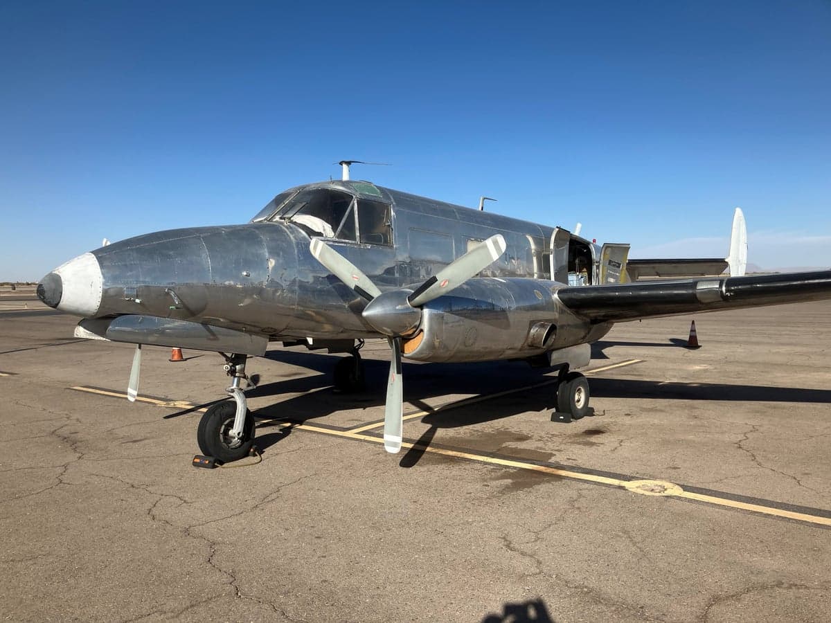 Side view of a silver Twin Bonanza aircraft on the tarmac.