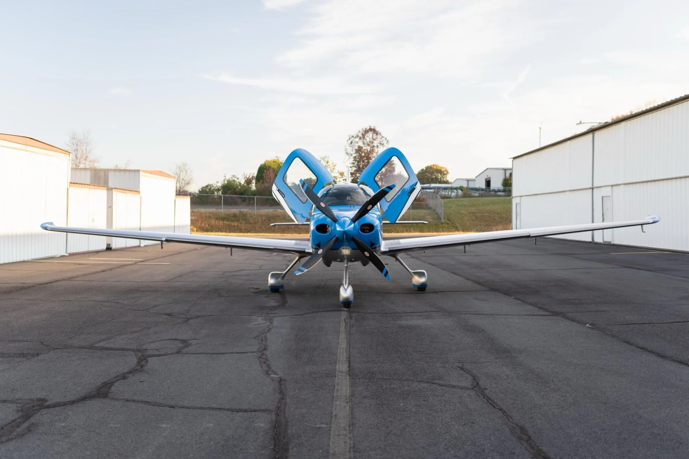A front view of the blue and silver Cirrus SR22T GTS aircraft, registration N79CV, with its gull-wing doors open, parked on an airfield.