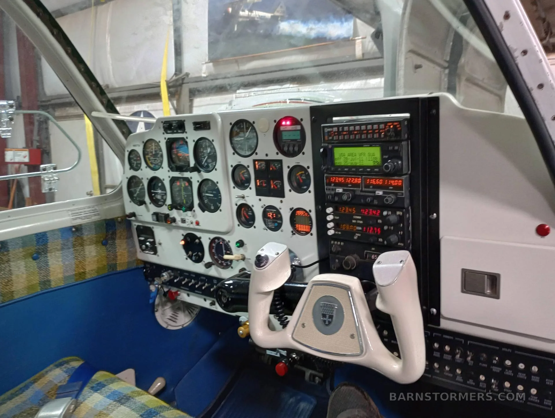 The cockpit of an aircraft showing the instrument panel, yoke, and blue and plaid interior.