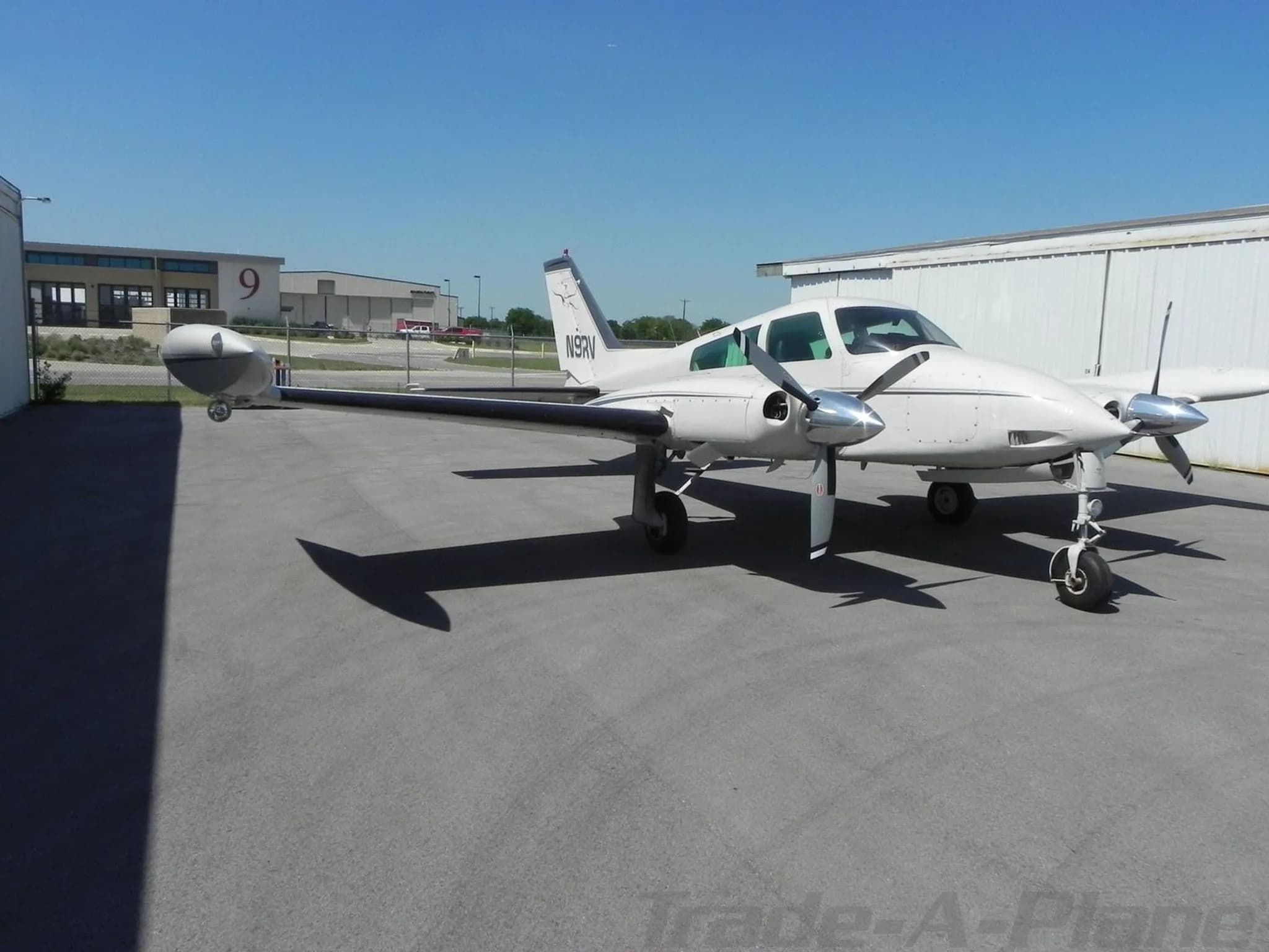 A three-quarter front view of a white twin-engine Cessna 310 aircraft with tail number N9RV parked on an asphalt apron.