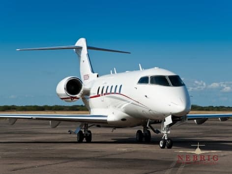 A white Bombardier Challenger business jet with red and grey stripes, registration N202DH, parked on an asphalt tarmac under a clear blue sky.