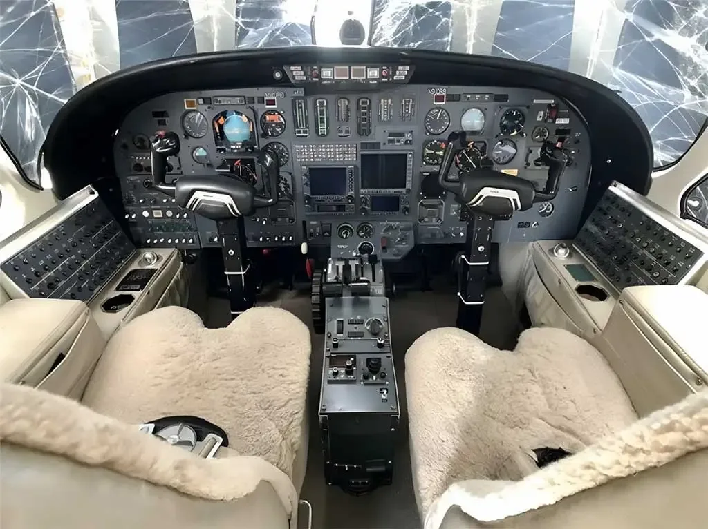 The cockpit of a business jet featuring a detailed instrument panel, dual yokes, and sheepskin-covered pilot seats.