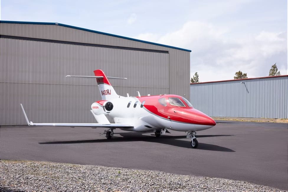 Side view of a red and white HondaJet N430HJ parked on the tarmac.