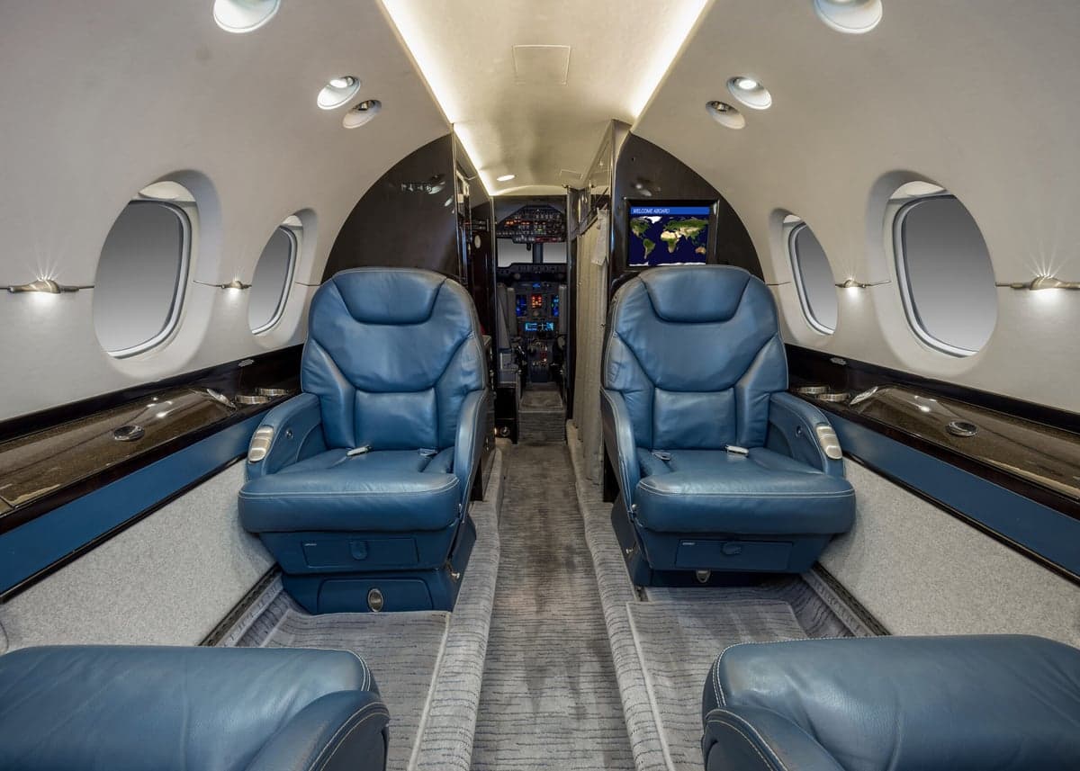 View of the aircraft interior featuring blue leather seats and a monitor displaying a world map.