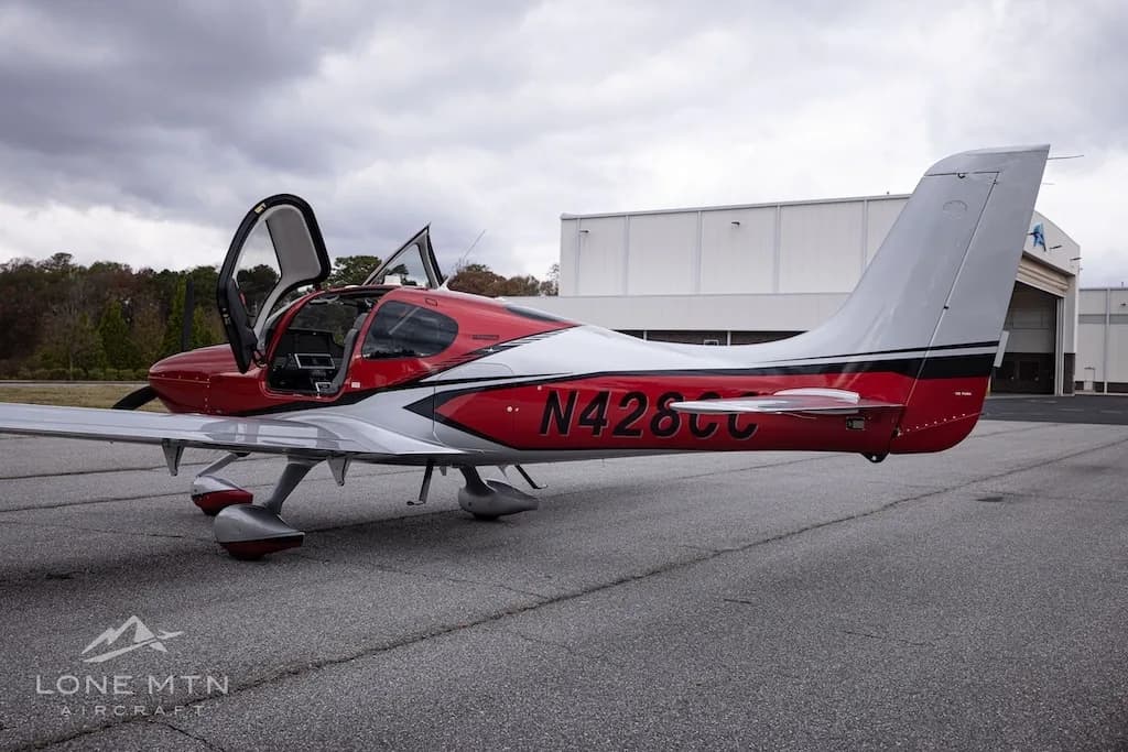A rear-side view of the red and silver Cirrus Vision Jet (N428CC) with its doors open, parked on an asphalt tarmac.