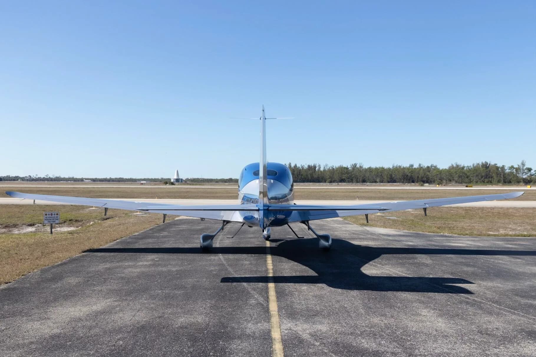 A rear view of a blue and silver Cirrus SR22 aircraft (N515SC) parked on an airfield with a runway in the background.