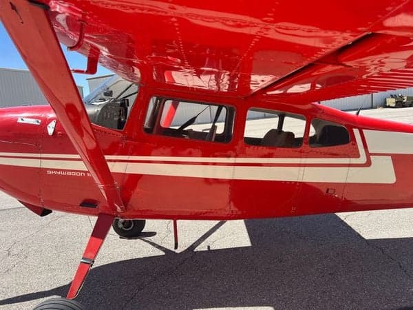 Close-up of the red and white Cessna Skywagon 180's side, showing the cabin and wing strut.