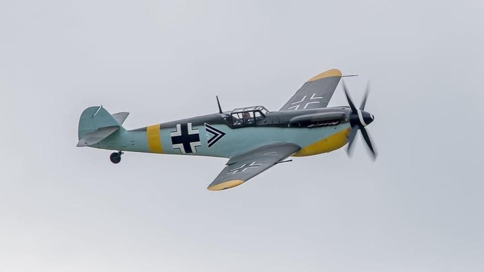 Top-down view of a Messerschmitt Bf 109 aircraft in flight, with fields below.