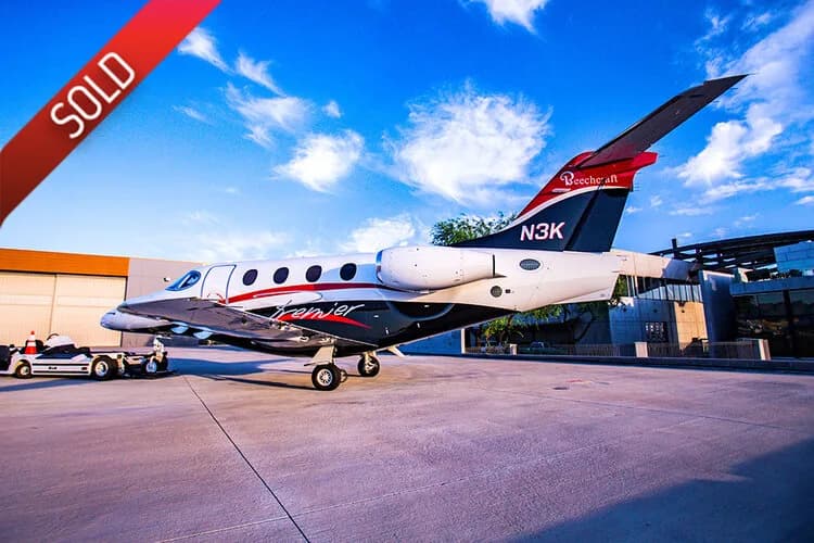 A white, black, and red Beechcraft Premier jet with registration N3K parked on an airport tarmac under a blue sky.