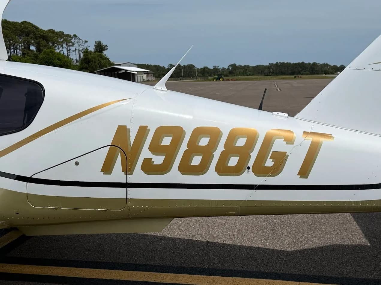 A close-up view of the gold "N988GT" registration on the white and gold fuselage of the Socata TB-20 Trinidad aircraft.