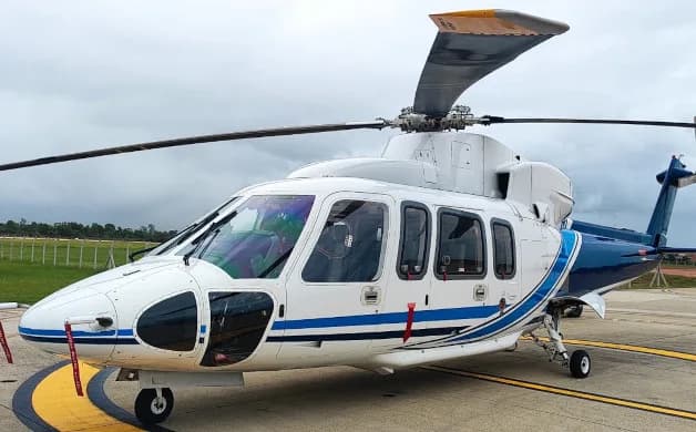 A white and blue executive helicopter, likely an AgustaWestland AW139, parked on an airfield under a cloudy sky.