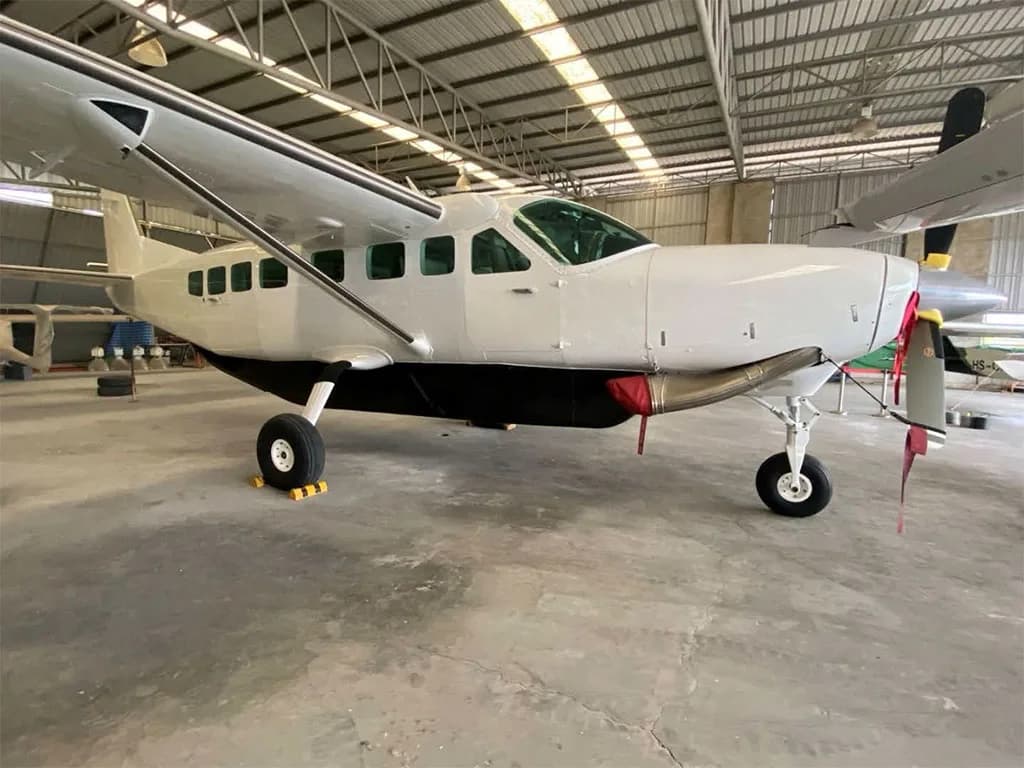 A white Cessna 208B Grand Caravan EX with a cargo pod is parked inside a hangar.