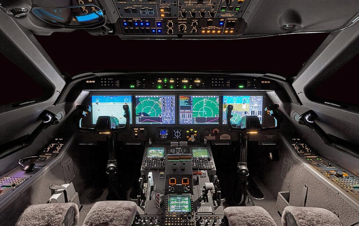A modern aircraft cockpit with multiple digital displays, control panels, and pilot seats, illuminated in a dark setting.