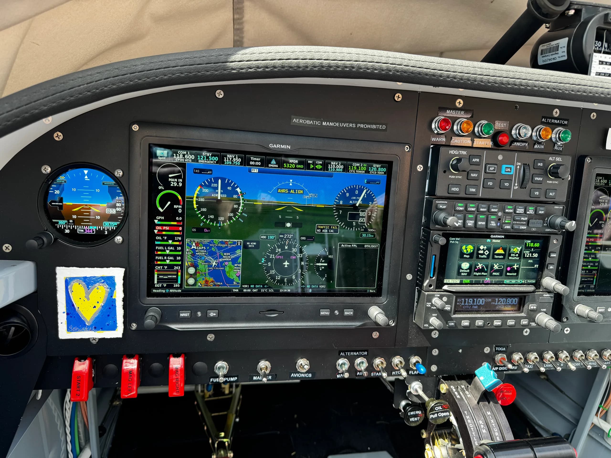 A close-up of the aircraft's instrument panel, displaying a large Garmin screen with flight data and a small yellow and blue heart sticker on the left.