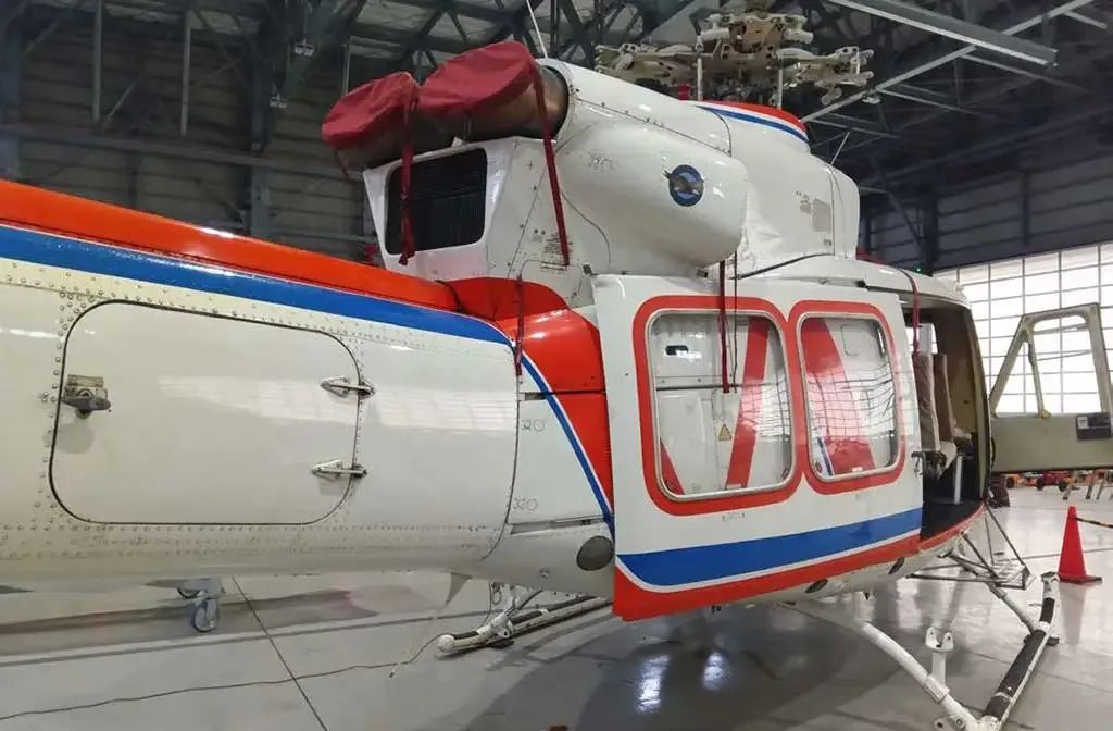 The rear-right side of a white helicopter with red and blue stripes, parked in a hangar with its door open.